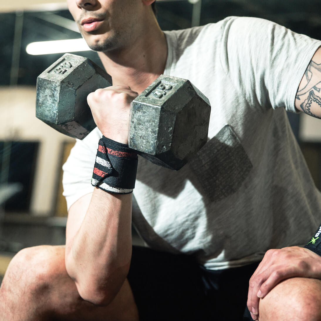 man doing one armed barbell raises with stars and stripes Man doing bench press with heavy barbell while wearing Bear KompleX Wrist Wraps