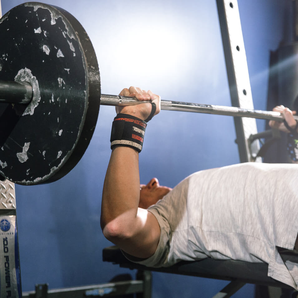 man benching heavy weight and wearing stars and stripes wrist wraps